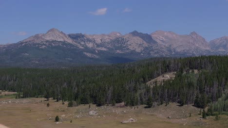 aerial trucking pan of evergreen forest on edge of grassy plains, big sandy trailhead in wind river wilderness, wyoming, with green fields, forests, and distant mountain ranges