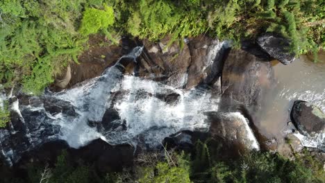 Dron-Con-Cámara-Hacia-Abajo-Haciendo-Movimientos-Ascendentes-Y-Descendentes-De-Una-Hermosa-Cascada,-Aguas-Que-Fluyen-Y-Naturaleza-Exuberante-Alrededor