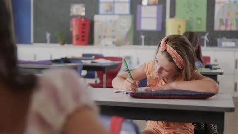 escolares diversas que escriben en los escritorios en la clase de escuela primaria, en cámara lenta
