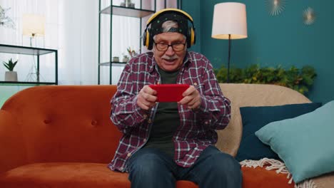 worried funny senior old grandfather man playing shooter online video games on mobile phone at home