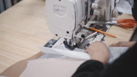 primer plano de una persona que pasa tela blanca a una máquina de coser de mesa, dentro del taller
