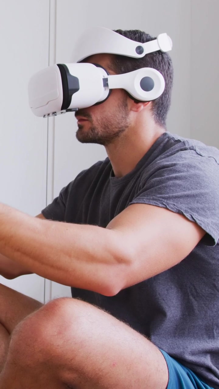 Video verticale: Uomo che mette su e regola il visore VR bianco a casa, testando i controlli del gioco.