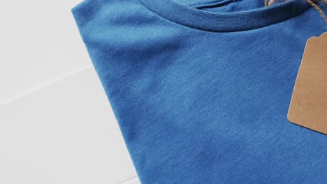 Video-of-flat-lay-of-blue-t-shirt-with-tag-and-copy-space-on-white-background