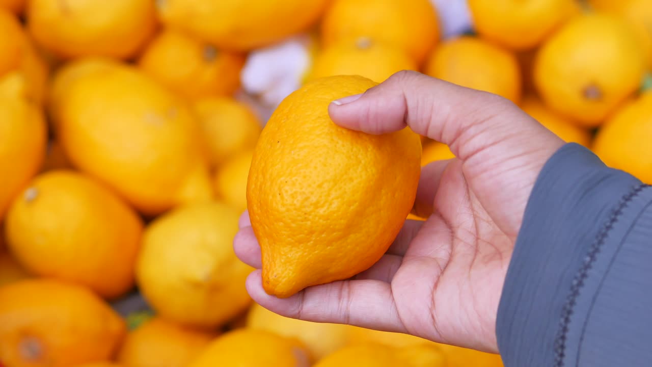 mano sosteniendo un limón, rodeado de limones