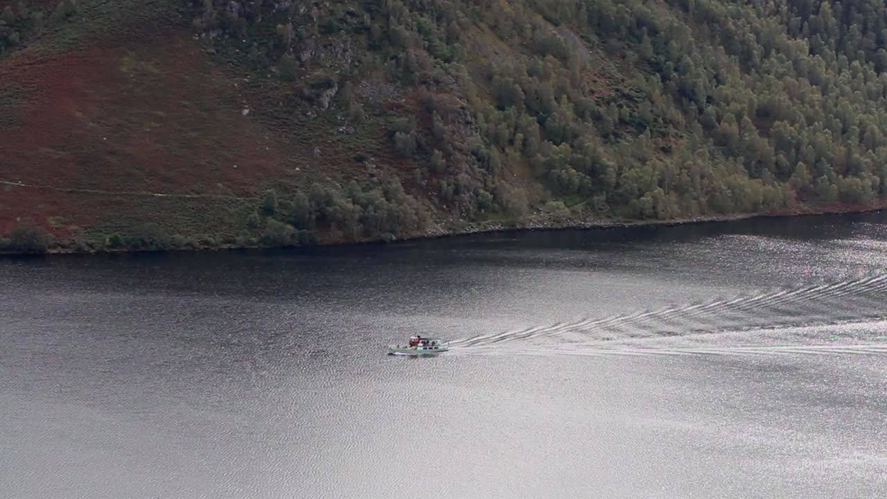 свет отражается от воды в национальном парке лейк-дистрикт с небольшой лодкой, оставляющей волны