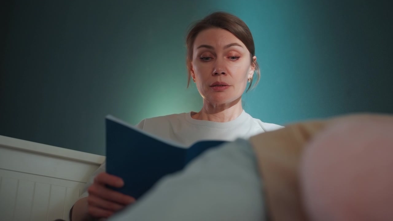 Kaukaski korepetytor czytający na głos z niebieskiej książki, ujęcie z niskiego kąta, perspektywa leżącego studenta, blask lampki nocnej, turkusowa ściana w tle, skupiony wyraz twarzy podczas nauczania wymowy i gramatyki w przytulnym otoczeniu.