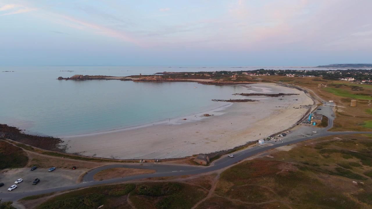 Baia di Lancresse, Guernsey, Isole del Canale. Filmato lento con drone ad alta quota all'ora d'oro di tutta la Baia di Lancresse, sopra la spiaggia, il lungomare, il caffè sulla spiaggia e l'adiacente Lancresse Common e campo da golf.