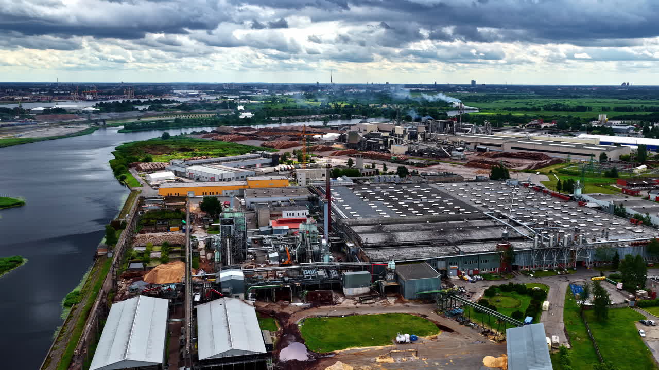 Wide aerial view of sawmill industrial area with river and log piles in Latvia