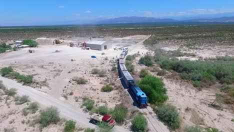 Un-Tren-Azul-Cruzando-El-árido-Paisaje-En-Argentina,-Con-Montañas-Al-Fondo,-Vista-Aérea