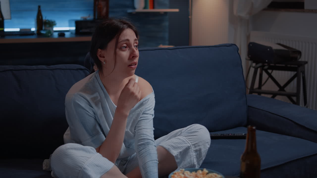 Sensitive woman watching drama movie on tv crying sitting on sofa