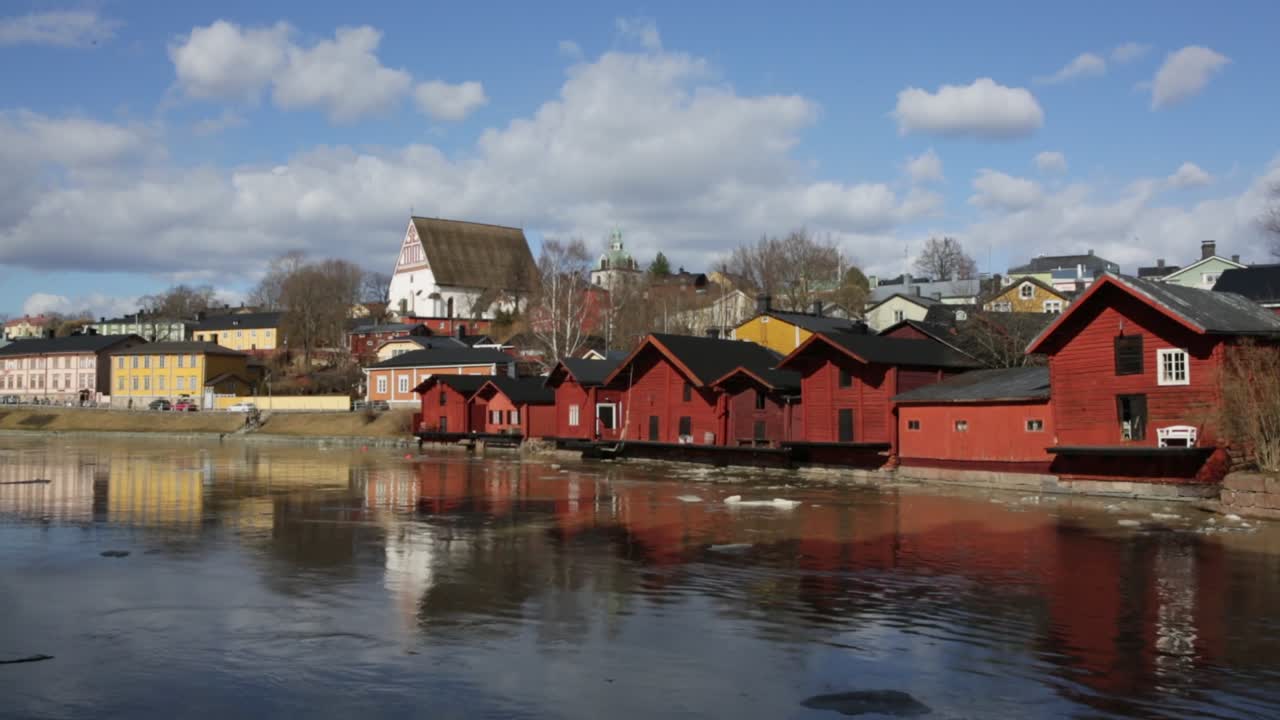 Droneutsikt over Gamle Porvoo, Finland, med historiske røde trelagerbygninger langs en rolig elv, refleksjoner på vannet og tradisjonell arkitektur ved elvebredden