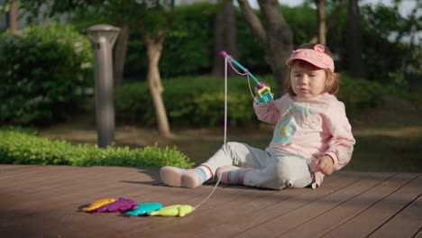 multi-ethnic little girl plays with a magnet fishing rod toy while sitting on the floor