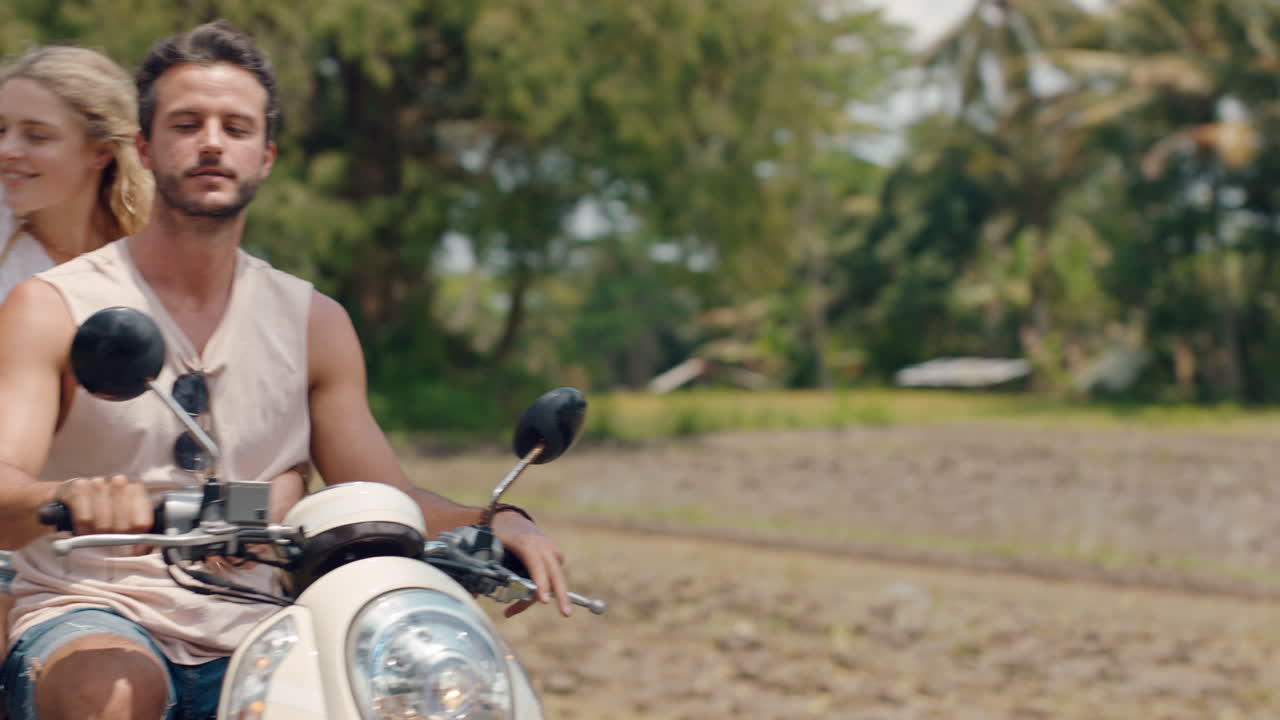 열대 섬에서 스쿠터를 타는 재미있는 커플 행복한 여성은 팔을 들고 축하하고 오토바이 타는 남자친구와 함께 휴가 도로 여행을 즐기고 있습니다.