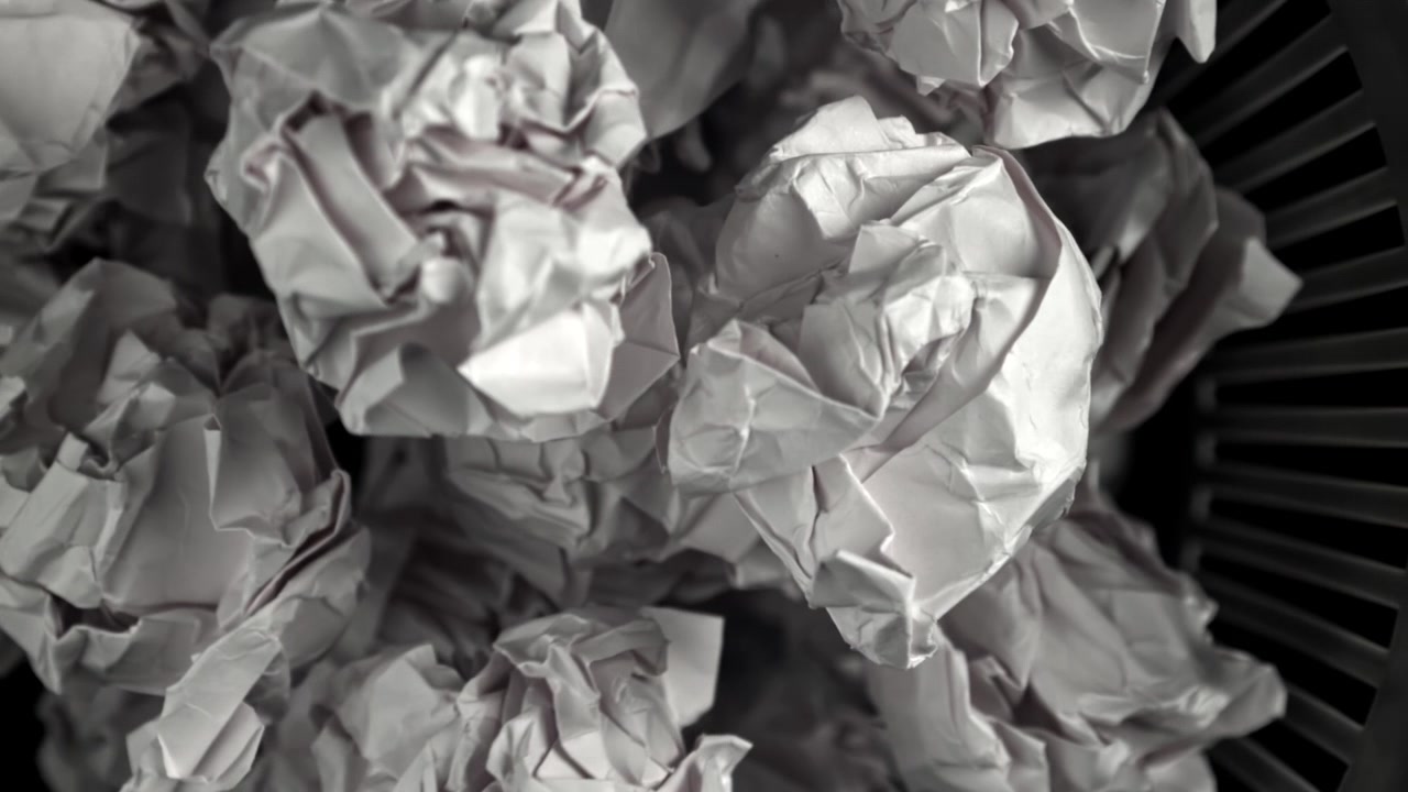Boules de papier blanc froissées dans une corbeille à papier noire