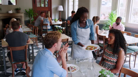 jong echtpaar in een druk restaurant dat maaltijden wordt geserveerd door een serveerster