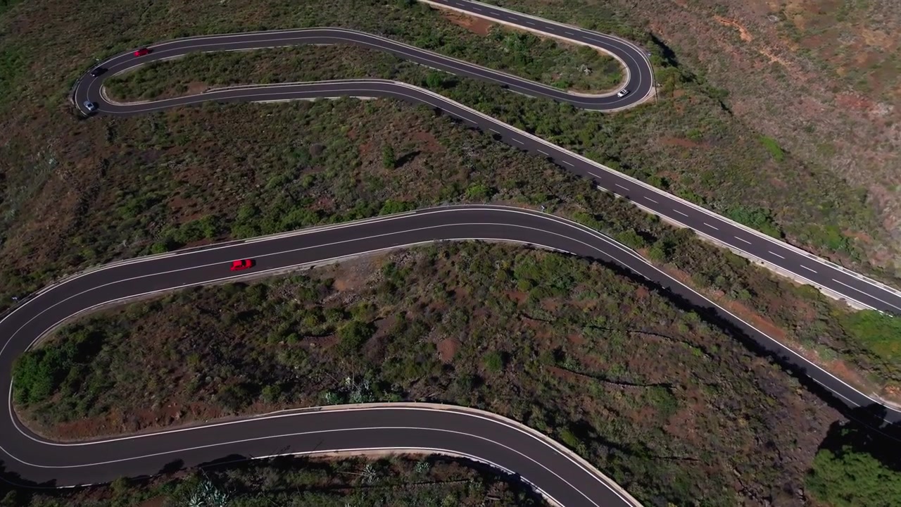 Vista aerea di una strada di montagna tortuosa con auto che attraversano terreno vulcanico e rovine.