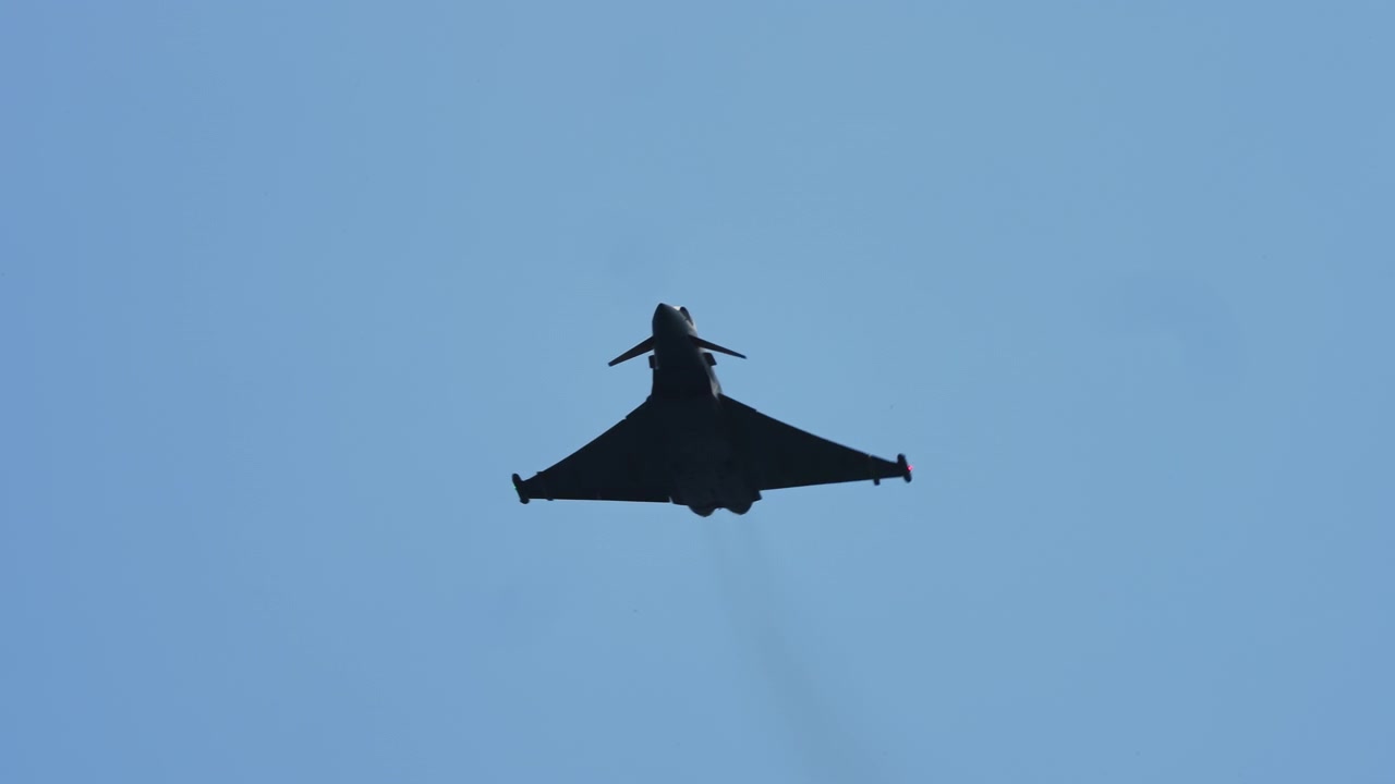 Military fighter jet performs sharp banking maneuvers and rolls high in the blue sky with clouds, captured in slow motion as it climbs