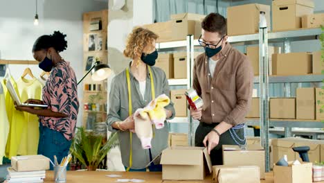 Caucasian-young-woman-and-man-working-in-clothing-shop-packing-parcels-while-african-american-woman-typing-on-laptop