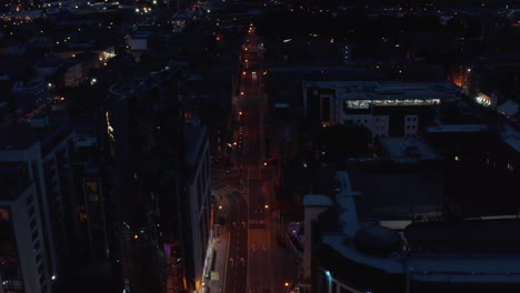 High-angle-view-of-low-traffic-on-straight-street-lit-by-street-lights.-Tilt-up-reveal-of-night-city.-Limerick,-Ireland