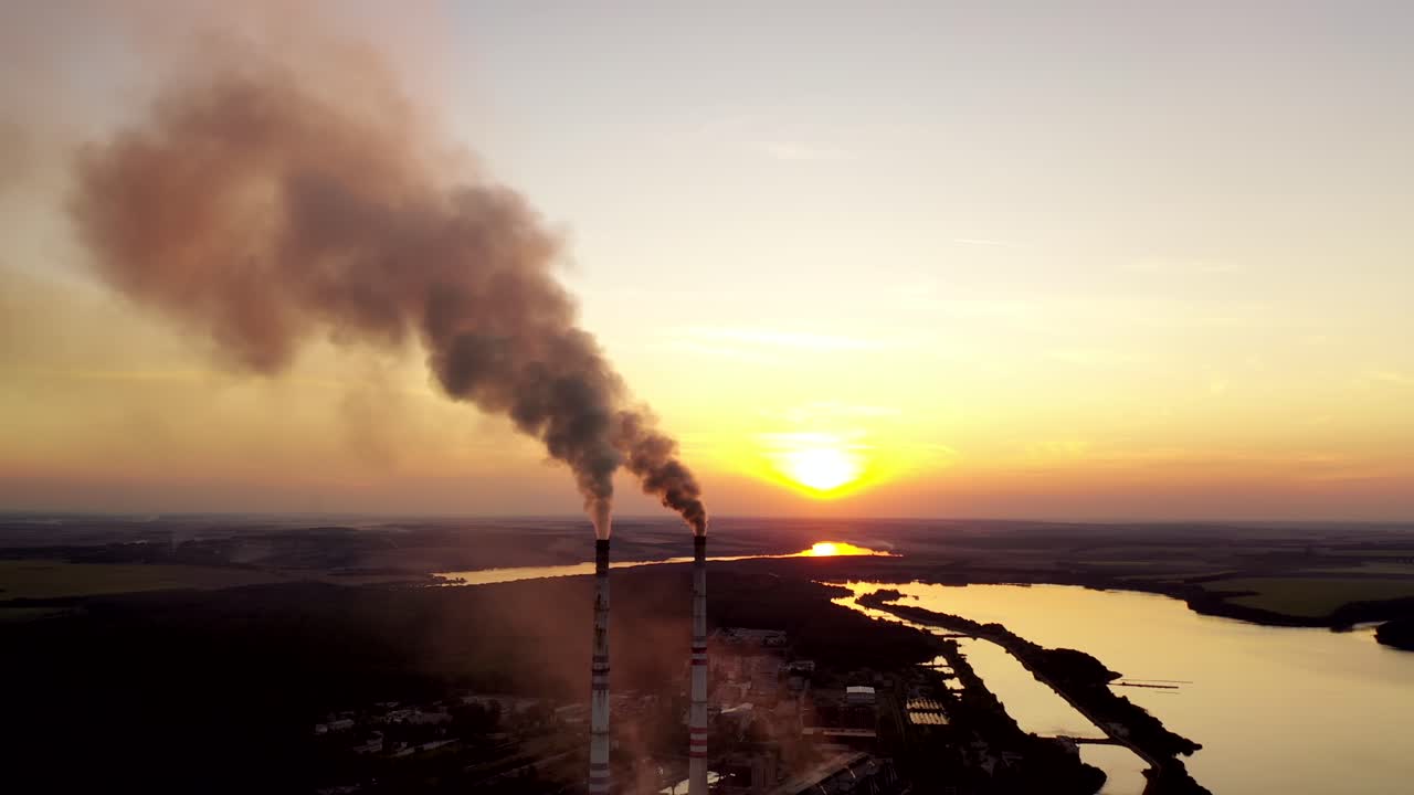 Industrial factory at sunset. Dirty smoke coming from pipes on the nature background in the evening. Manufacture near the river.