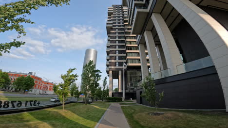 pov shot while waling along a path on the side of tall skyscraper office buildings beside a road on a sunny morning