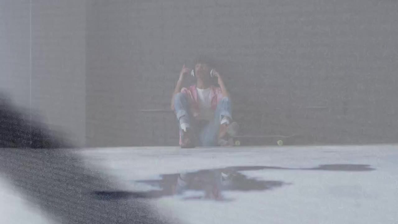 Vertical video: Glare shifting, man tuning headphones for music on skateboard in bay, sweatshirt