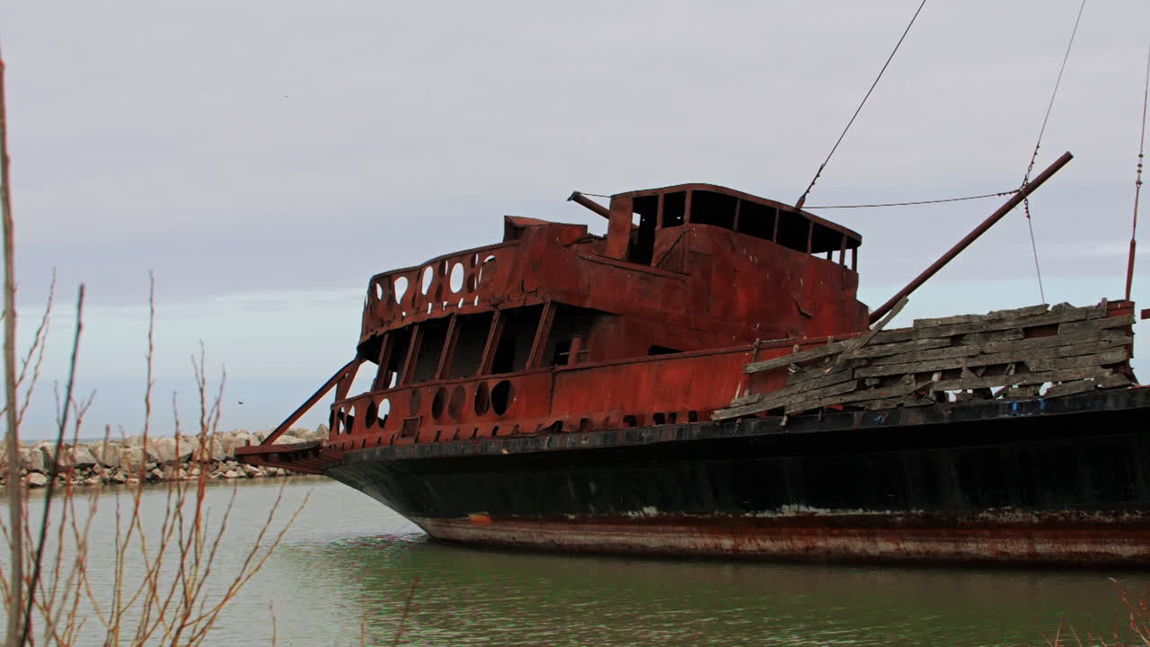 Rusty red shipwreck stuck in shallow green water