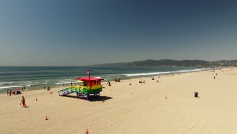 panoramic views of venice beach featuring a vibrant rainbow lifeguard tower, the ocean, and people enjoying the sunny day.