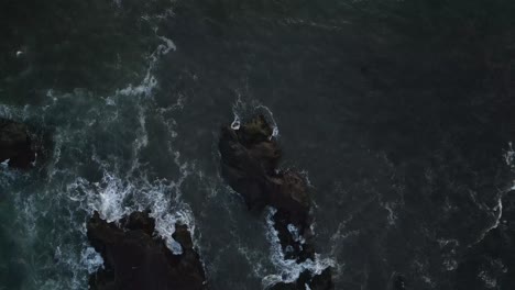 vista aérea de las olas blancas y las rocas monocromáticas oscuras del océano