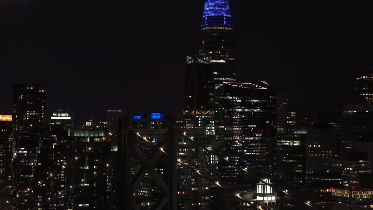 Salesforce Tower com luz de farol vermelha na ponte, horizonte denso e iluminado do centro da cidade, rua da cidade brilhante e céu noturno escuro. São Francisco, Califórnia, EUA. Tomada aérea ampla. Passando. Cena tranquila