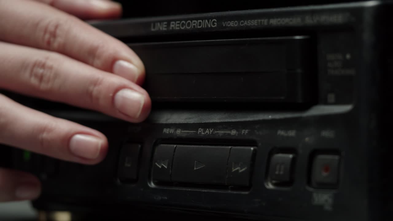 Mano che inserisce una cassetta VHS in un vecchio videoregistratore a cassette e preme riproduci.