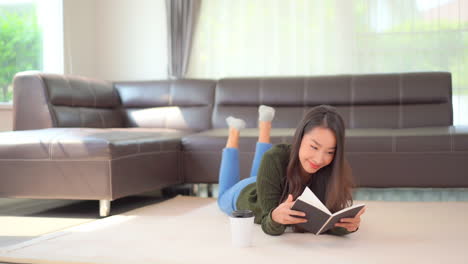 young brunette girl is reading a book or a textbook lying on a floor