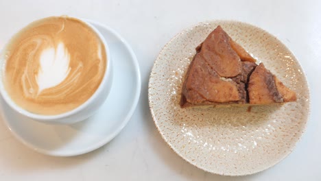 coffee with latte art and a slice of cake on a white table