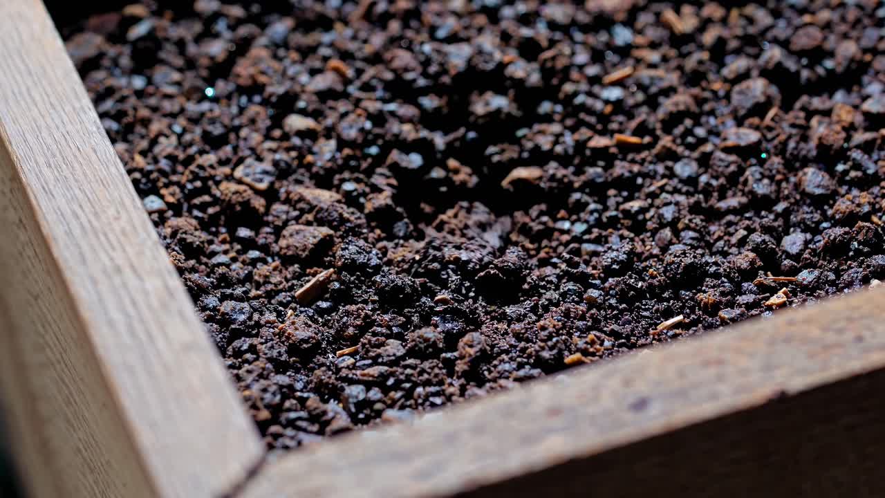 Close-up video of rich, dark soil in a wooden planter, shot from a low angle, highlighting texture