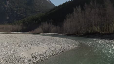 drone footage flying over a green blue river moving around a river bend with mountains in the background 4k footage