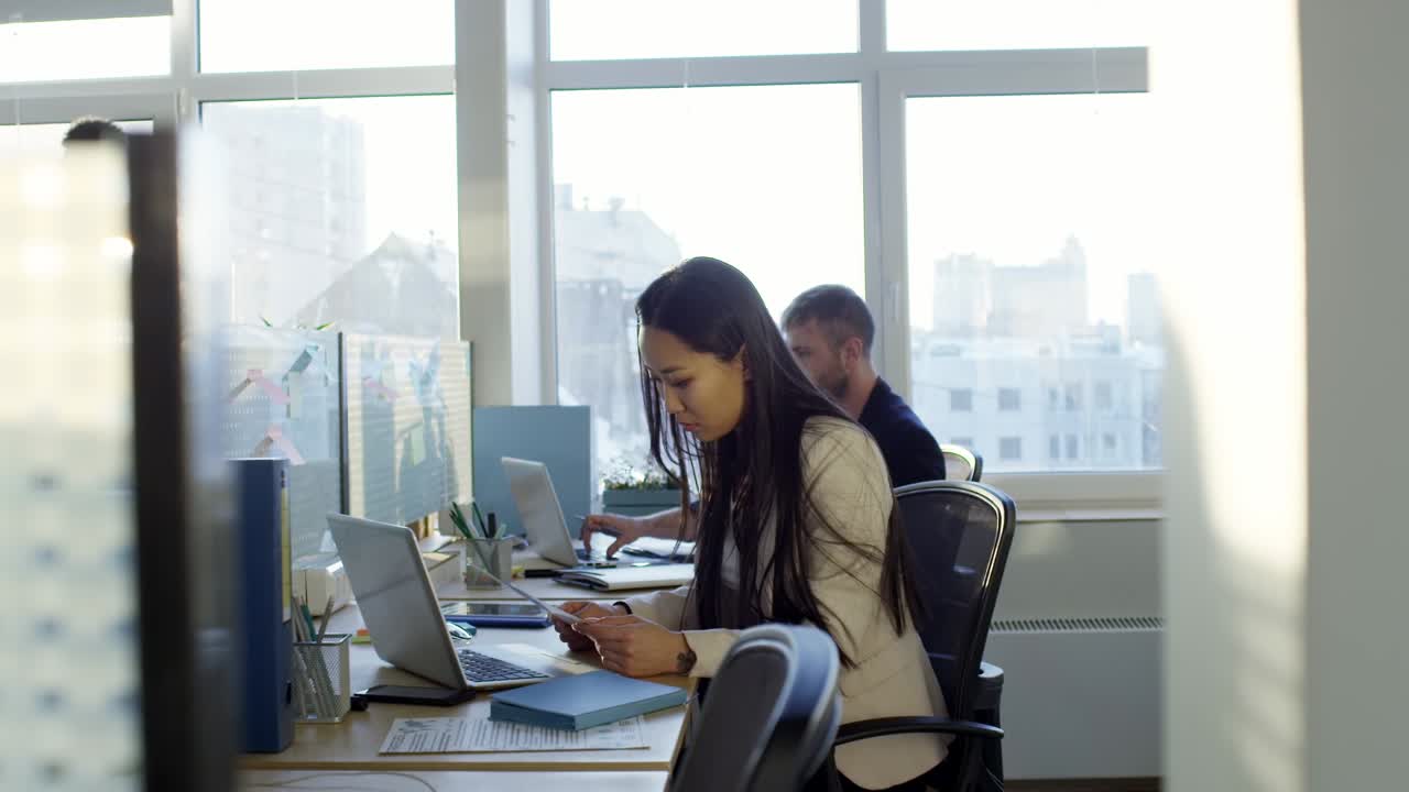 Joven asiática trabajando con colegas en una oficina de espacio abierto