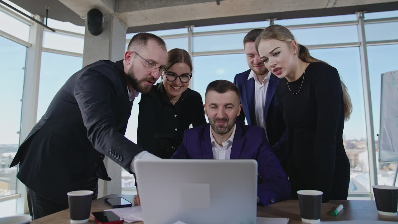 Colleagues gathered around laptop. Workmates point at the computer and discuss their working issues. Gradual close up to the coworkers.