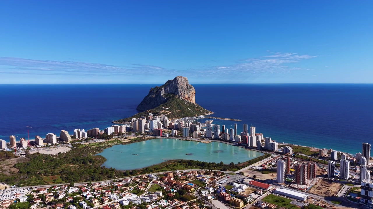 Città costiera di Calpe ad Alicante, Spagna, con l'iconica formazione rocciosa Penon de Ifach che si erge sul Mar Mediterraneo, marina, laguna e skyline urbano.