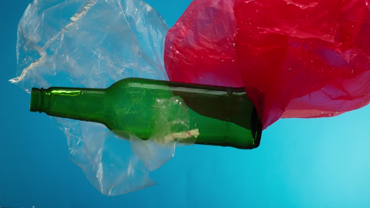 Plastic zakken en glazen fles drijvend in water