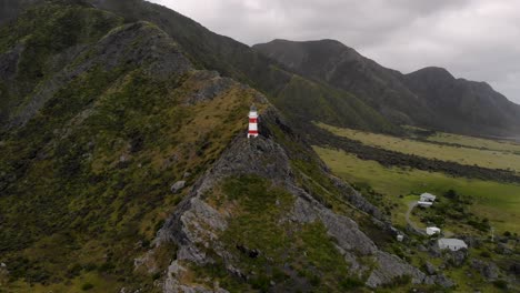 Drone-Vuela-Hacia-El-Faro-De-Cape-Palliser-Con-Vistas-A-La-Montaña-En-Cape-Palliser,-Nueva-Zelanda