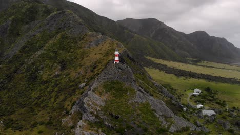 drone vuela hacia el faro de cape palliser con vistas a las montañas en cape palliser, nueva zelanda