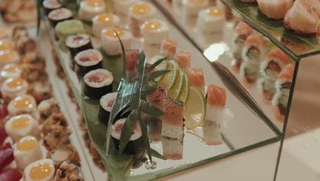assorted sushi rolls with salmon and lime slices presented on mirrored tray at sushi buffet