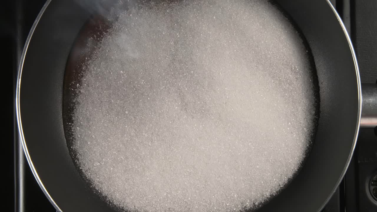 la velocidad rápida del azúcar se derrite en una sartén a fuego de gas y se convierte en caramelo revolviendo con una cuchara de madera