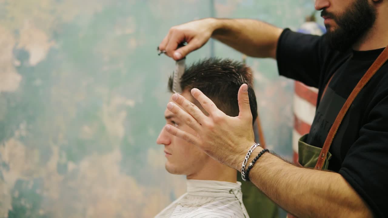 vista lateral de un joven hombre caucásico guapo con un piercing en la oreja secándose el cabello en una foto de barbero estilo retro
