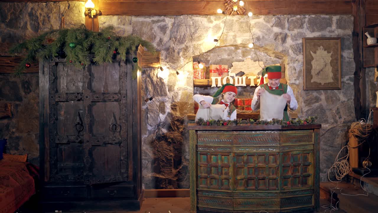 Elves inside the post office. Happy elves putting envelopes on the table in Christmas decorated room. New Year eve.