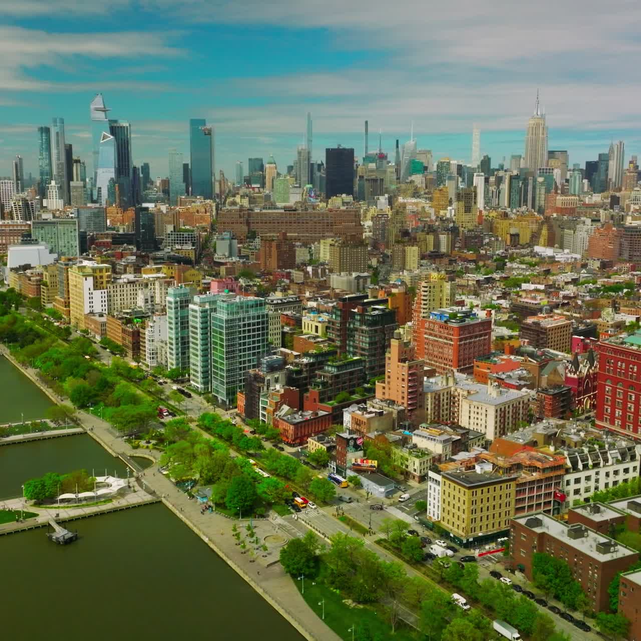 Colorful bright architecture of New York at sunny weather day. Beautiful parks at the waterfront of the river. Skyscrapers at backdrop