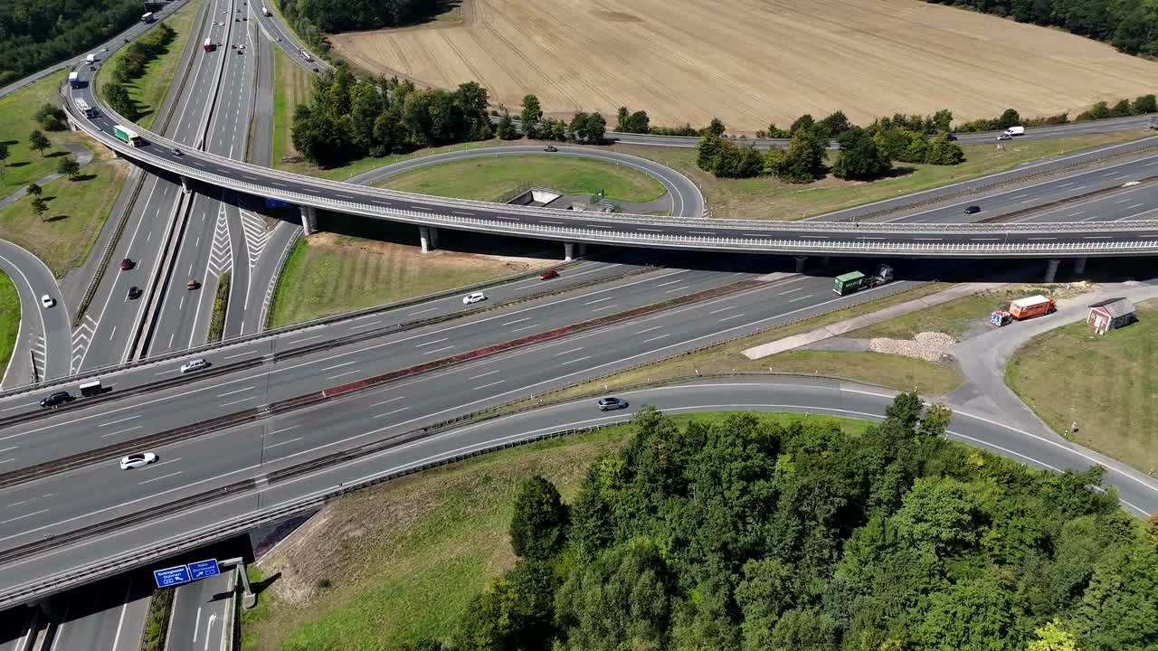 German autobahn highway interchange with traffic, overpass and surrounding fields, showing modern infrastructure and transportation system. Aerial lateral wide shot. Sunny summer day