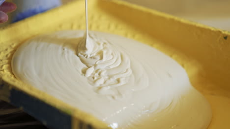 light paint for home renovation. worker pouring creamy color into a paint tray. apartment decorating and home construction. close-up.