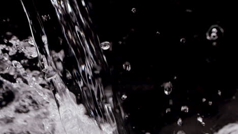 agua vertiendo en fondo negro en cámara lenta con salpicaduras refrescantes