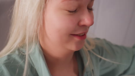 close up of blonde girl smiling with joy as she looks toward someone playfully hitting her with pillow, her expression captures warmth and laughter in cozy bedroom setting